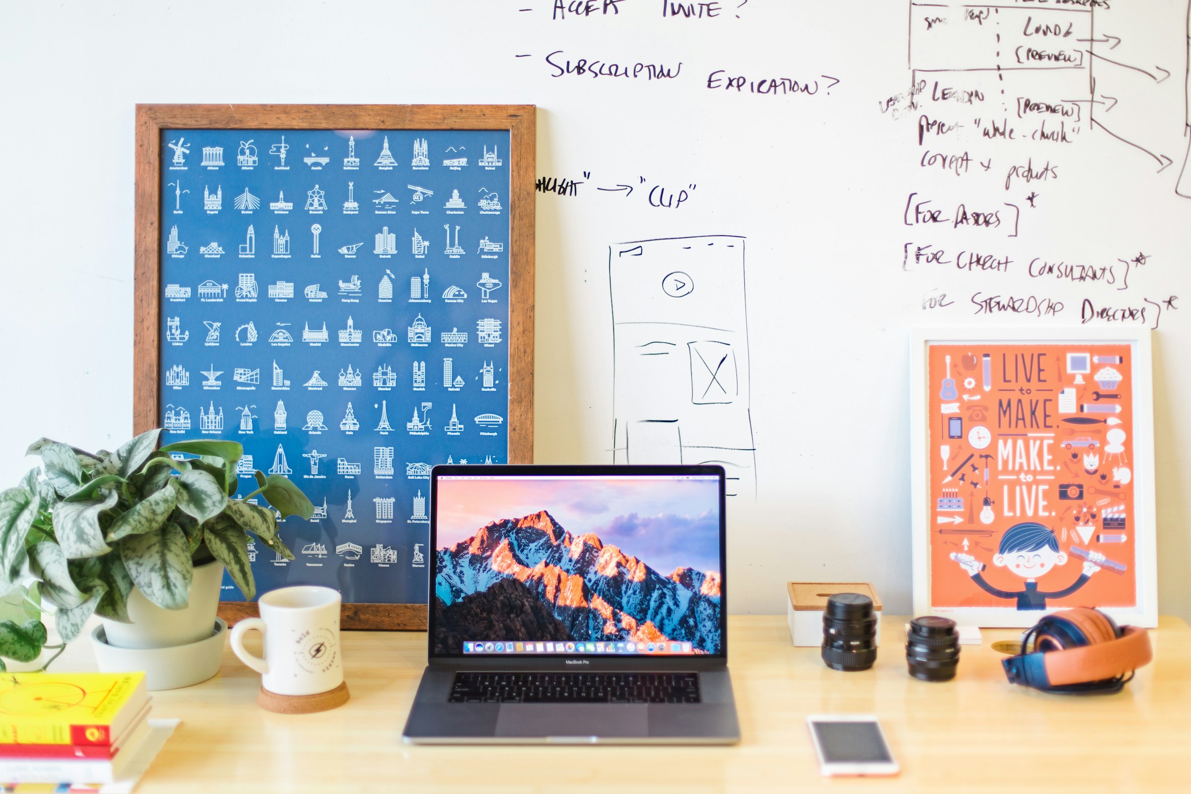 A designer’s desk with a laptop, sketching tools, plants and a whiteboard