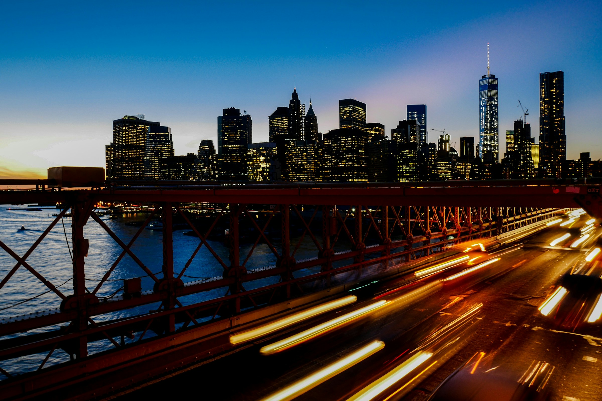 Long-exposure light trails sweeping past the New York skyline at dusk