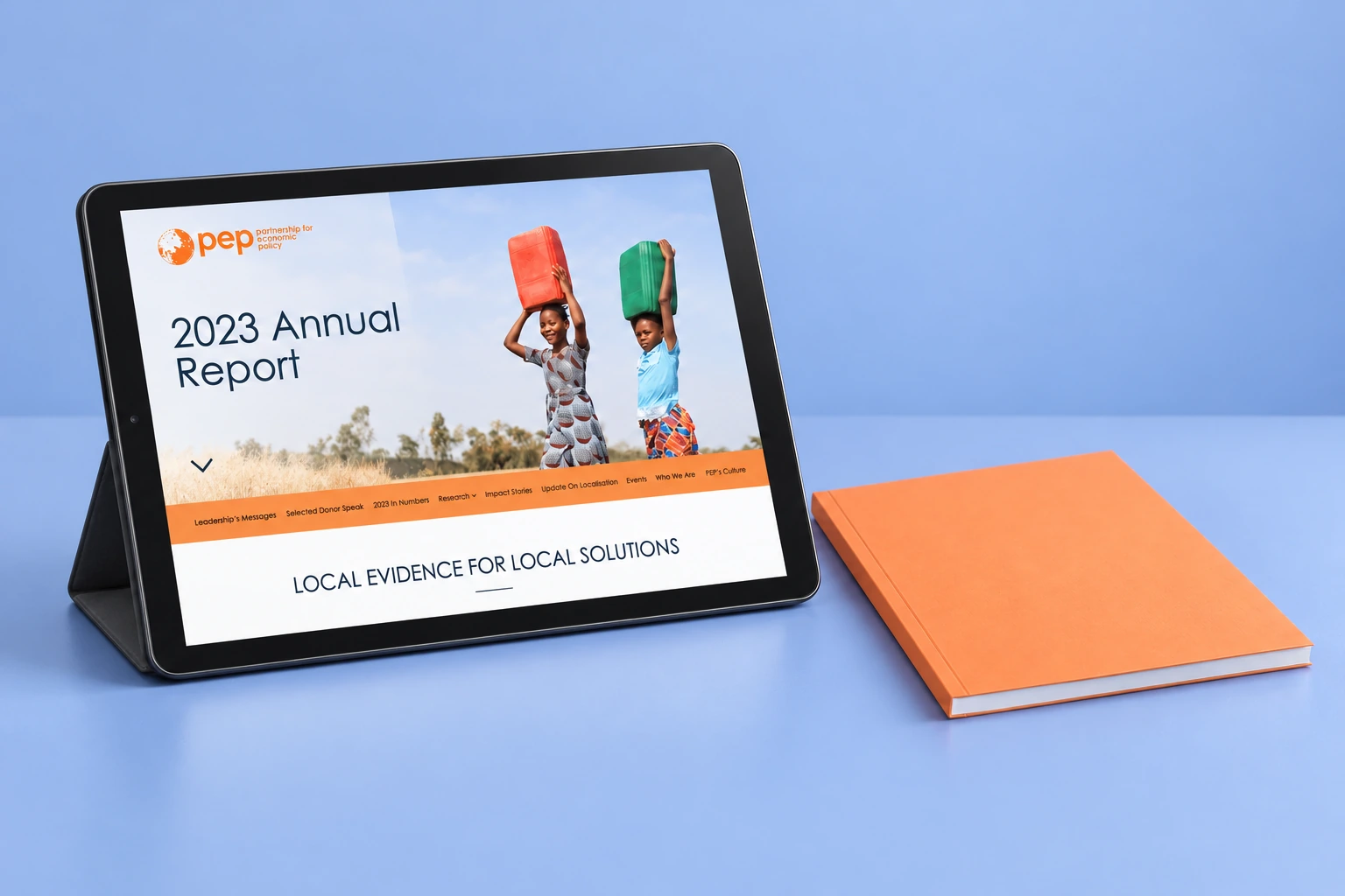 PEP digital annual report presented on a tablet beside an apricot-orange booklet against muted periwinkle